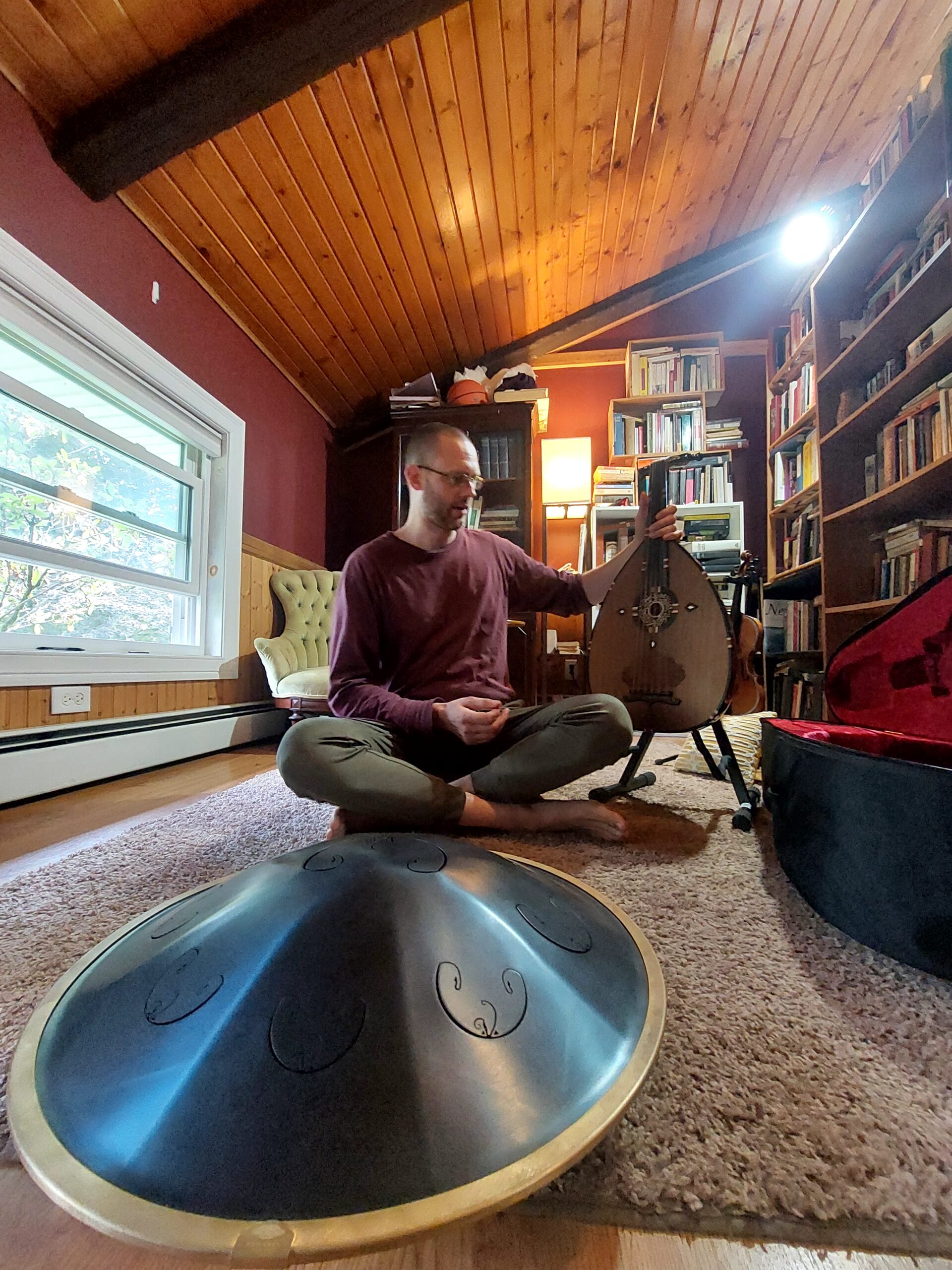 Adrian Paulsen seated barefoot in his library preparing to play Oud and Rav Vast.